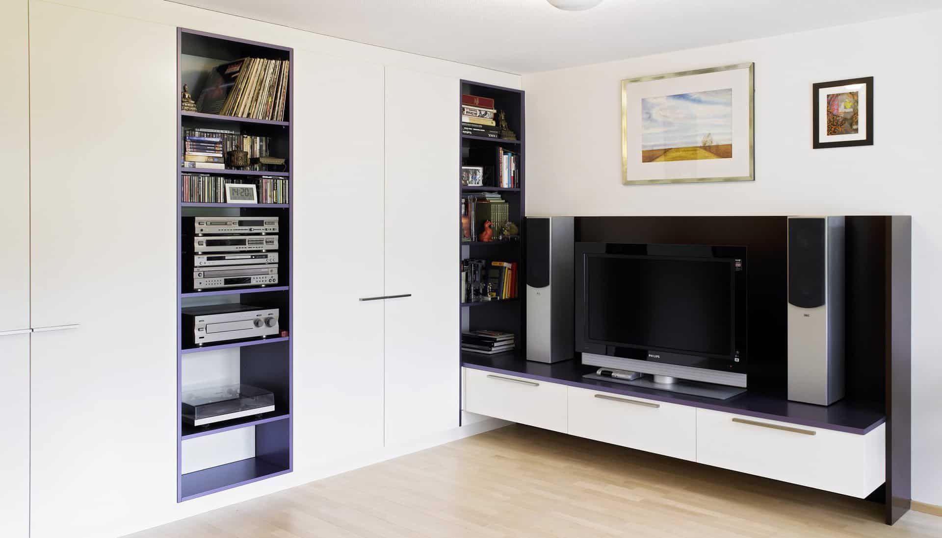 Modernes Wohnzimmer mit weißen Schränken, schwarzem TV-Möbel und eingebauten Regalen.