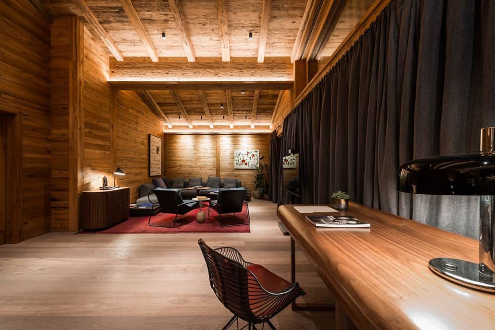Gemütliche Holzlounge mit Sofa, Teppich, Schreibtischlampe und dunklen Vorhängen in warmem Licht