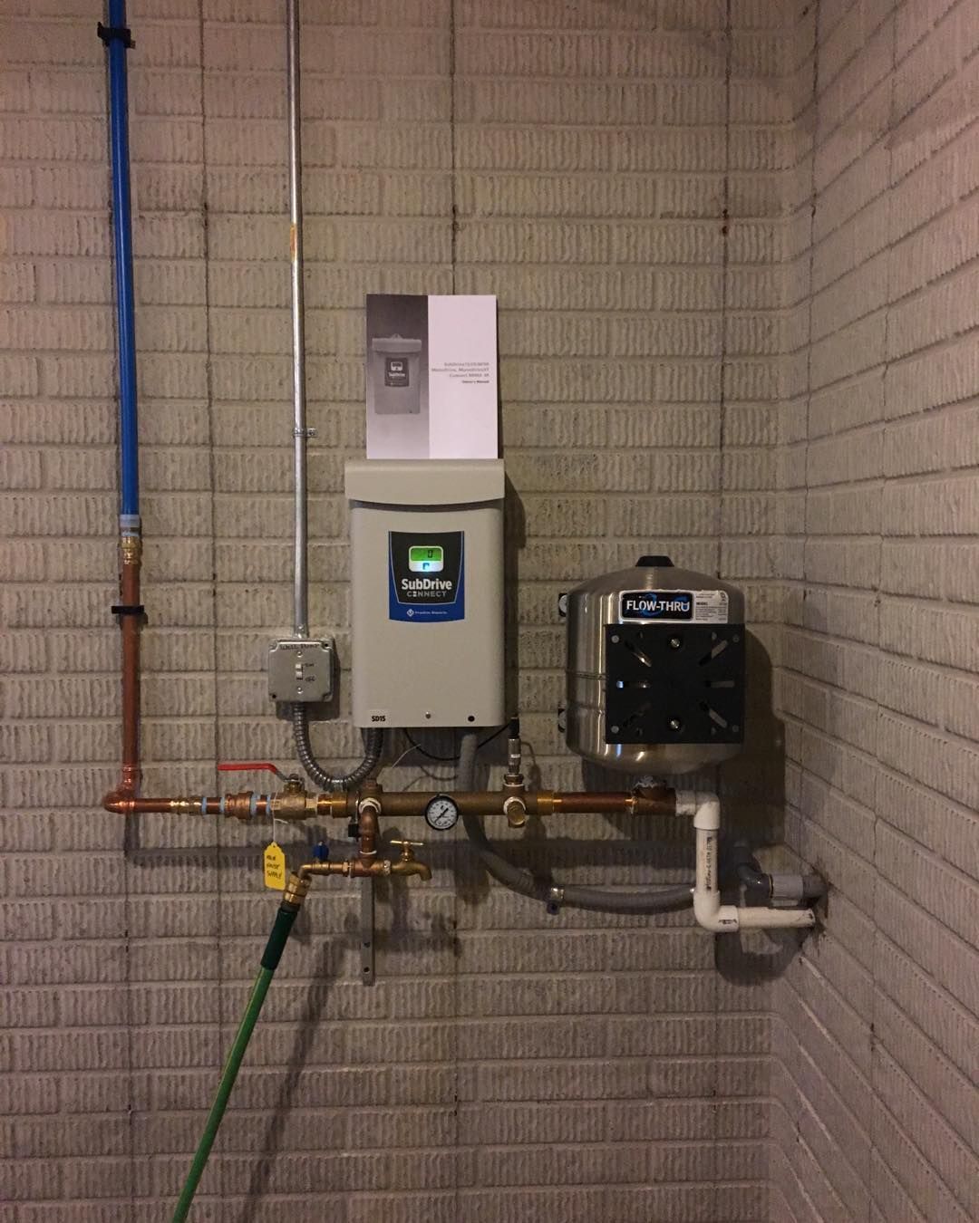 Water system components mounted on a brick wall: a control box, a filter, and pipes.