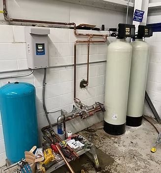 Water treatment system with blue pressure tank, two tall white tanks, and copper pipes against a white wall.