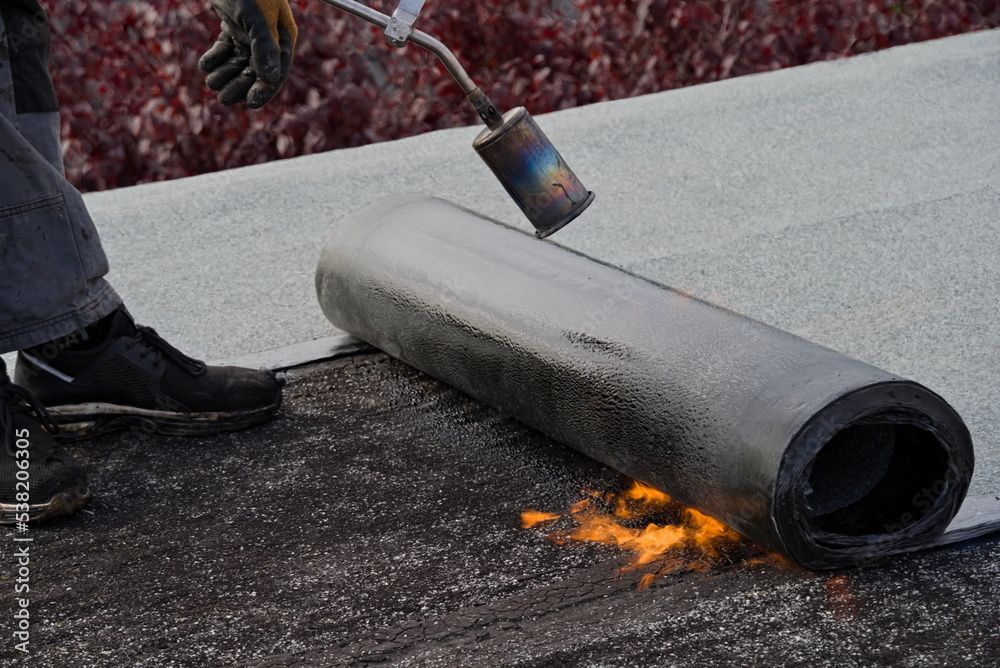 Personne utilisant un chalumeau pour installer un matériau de couverture sur un toit plat.