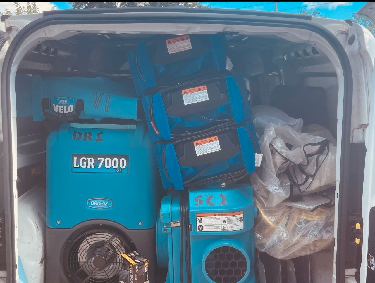 The back of a work van loaded with blue industrial dehumidifiers, air movers, and wrapped restoration equipment.