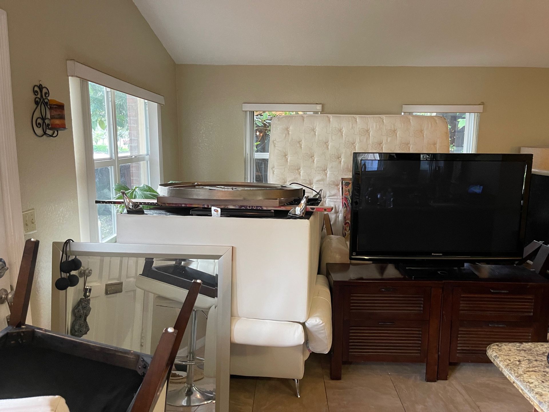 A room filled with furniture, including a large white tufted headboard, a television on a dark wood stand, and a mirror.