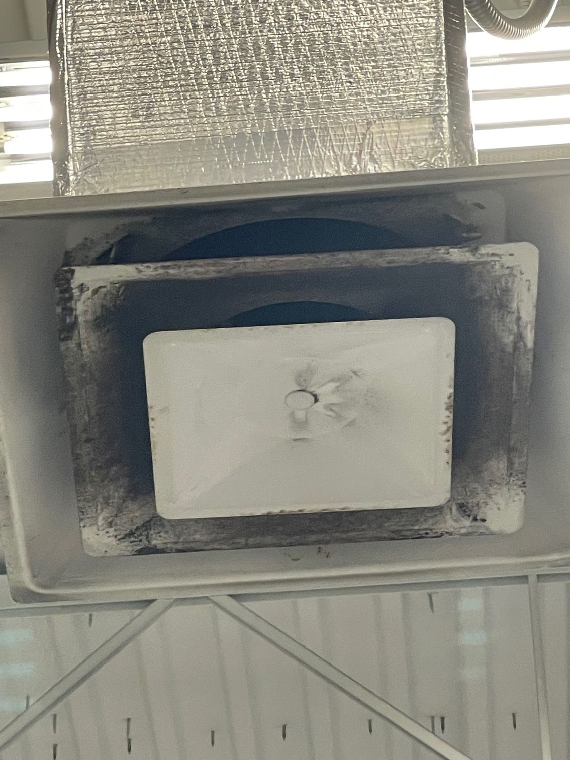 A close-up view of a dusty, rectangular ceiling vent or air conditioning register with a central white cover.