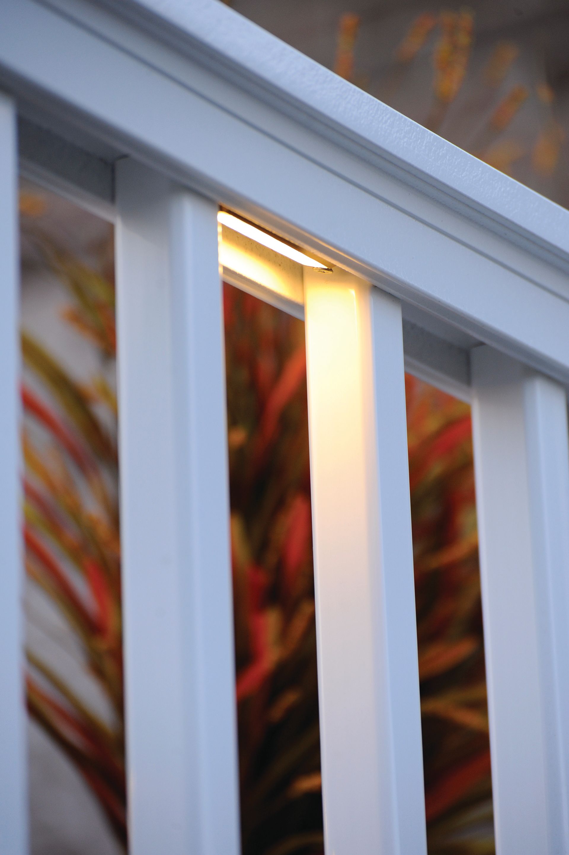 White stair railing with a warm lit post, in front of a blurred colorful background