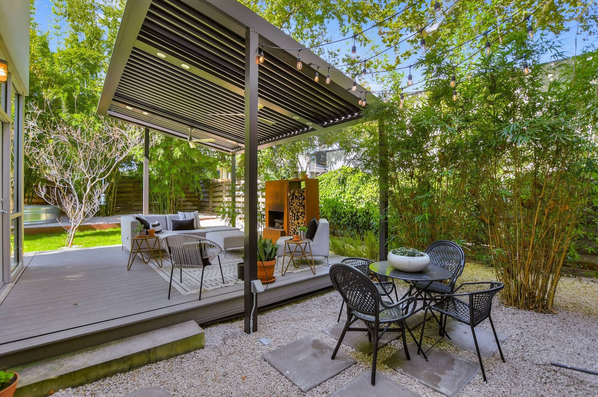 Covered patio with outdoor dining set, wicker chairs, and a small table beside bamboo greenery.