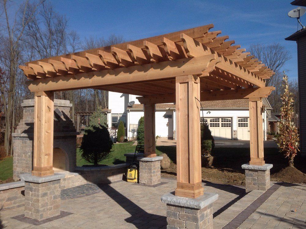 Wooden pergola structure with four posts on stone bases in a courtyard under clear skies
