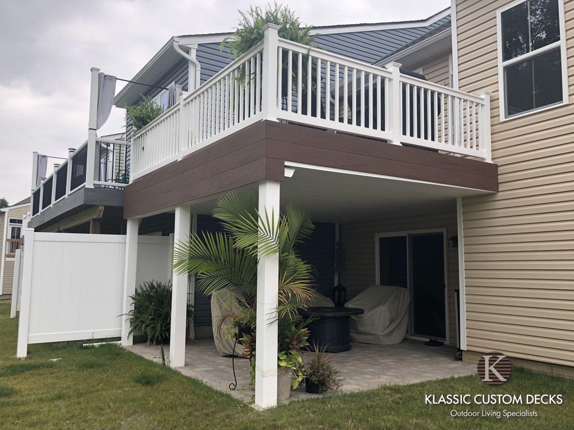 Raised deck with white railings and stairs over a patio beside a beige townhouse
