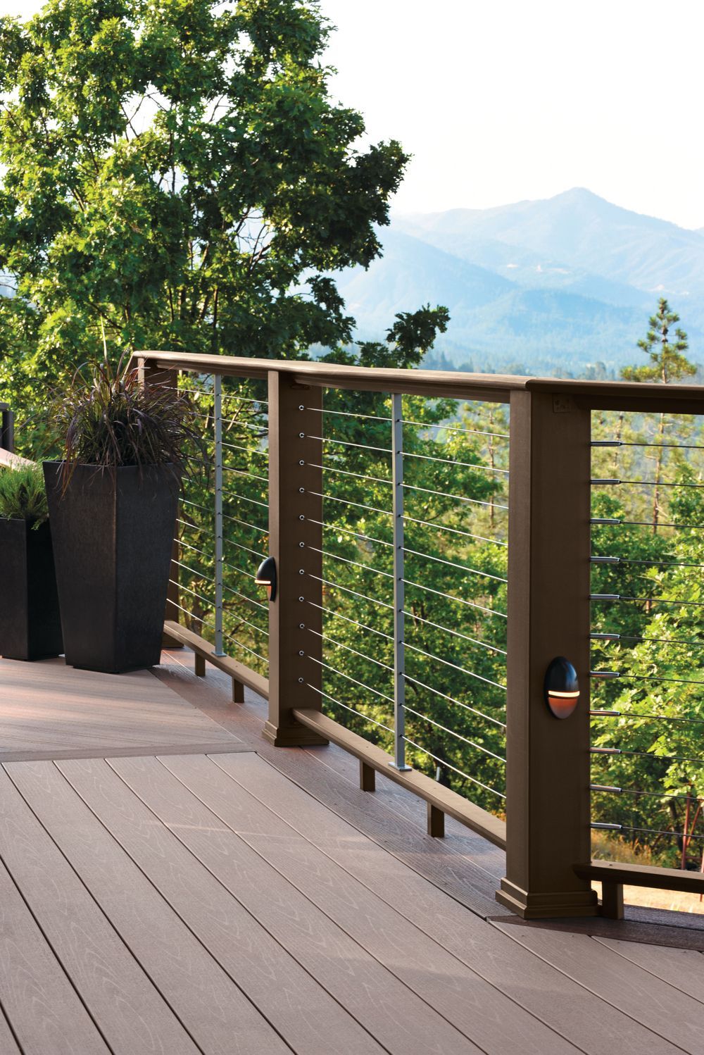 Wooden deck with railing overlooking trees and a hazy mountain view