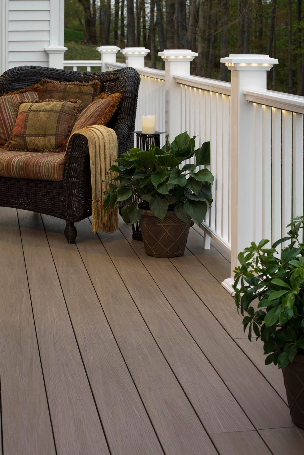 Wooden deck with wicker chair, potted plants, and white railing lights at dusk
