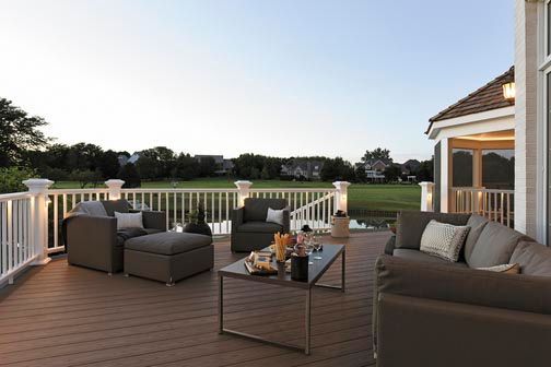 Patio with wicker seating and coffee table overlooking a green lawn at sunset