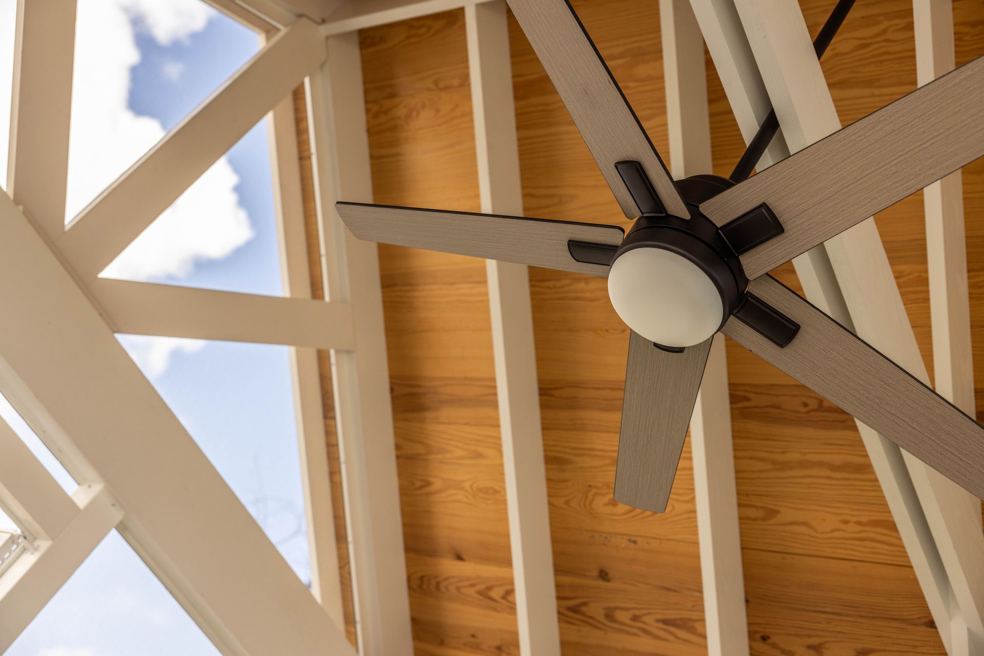 Ceiling fan on a wooden-beamed ceiling against white rafters and sky