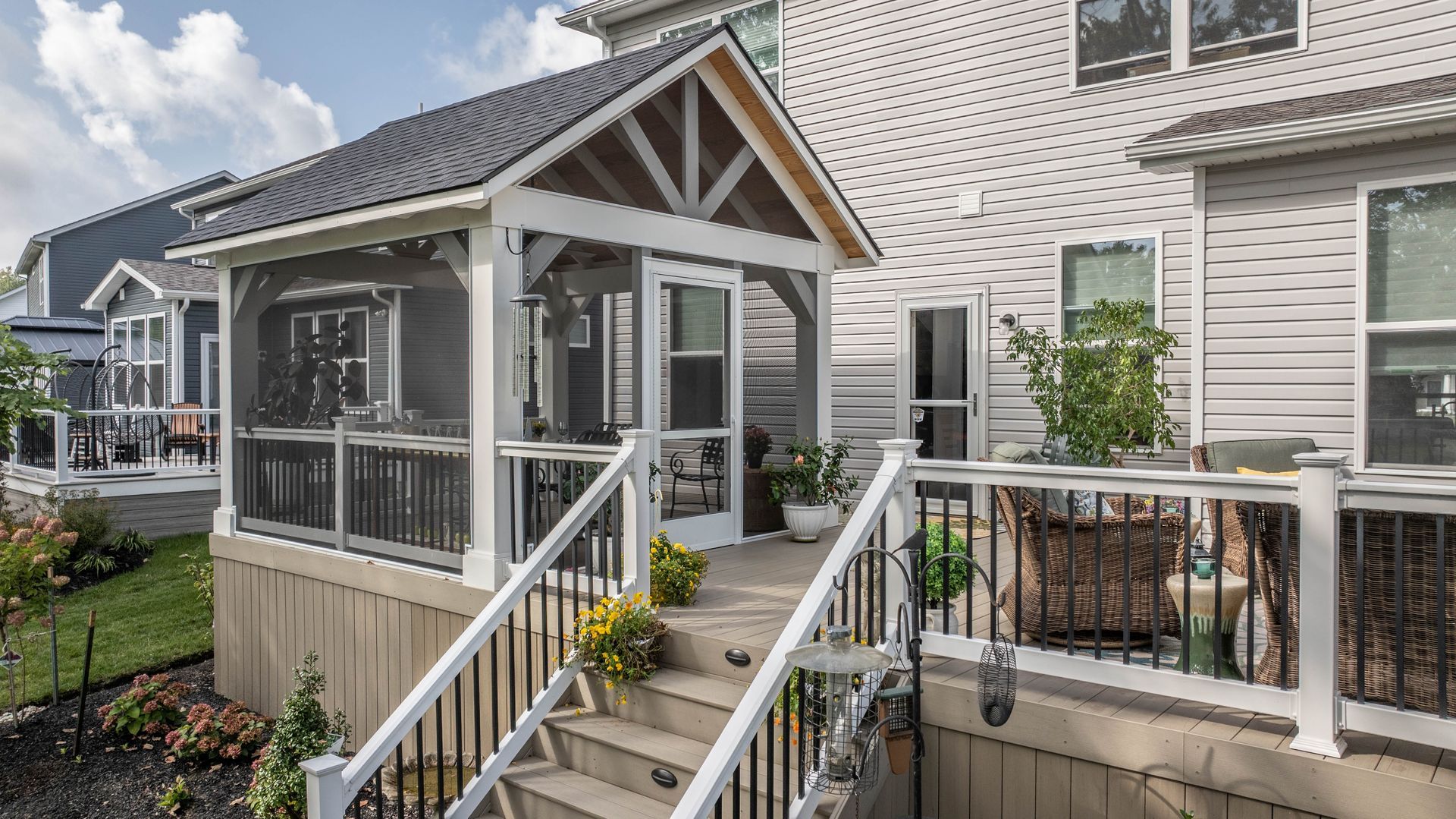 White cottage-style porch with stairs, railing, and potted plants in a sunny residential neighborhood