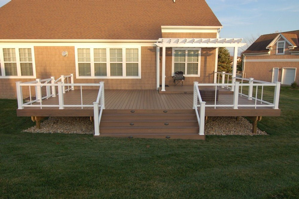 House with a wooden front deck, white railings, and a covered porch overlooking a lawn