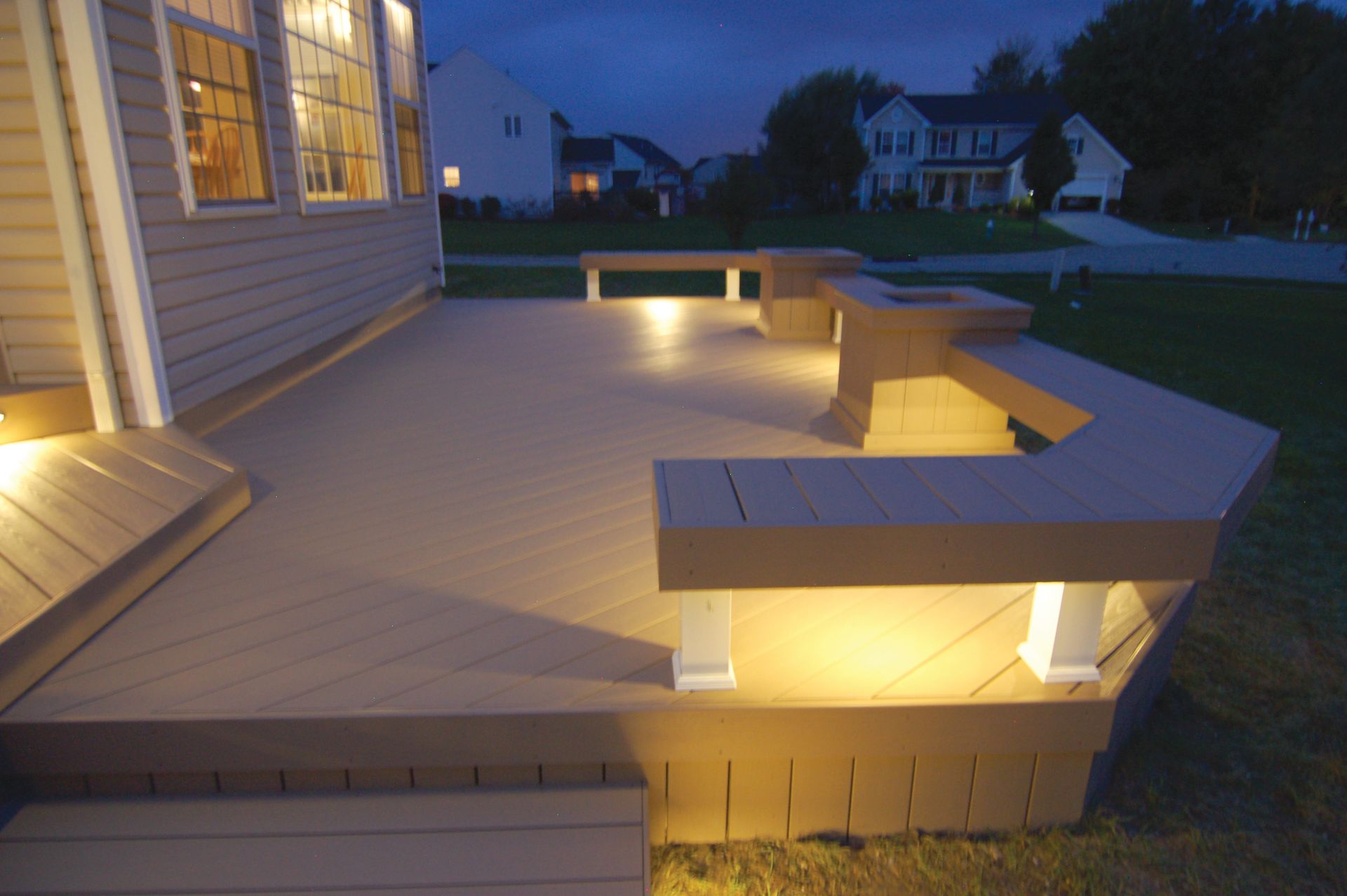 Backyard deck with built-in bench lighting glowing at dusk beside a house