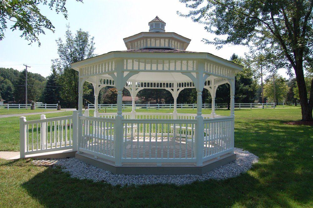 White gazebo in a sunny park with green lawn and trees