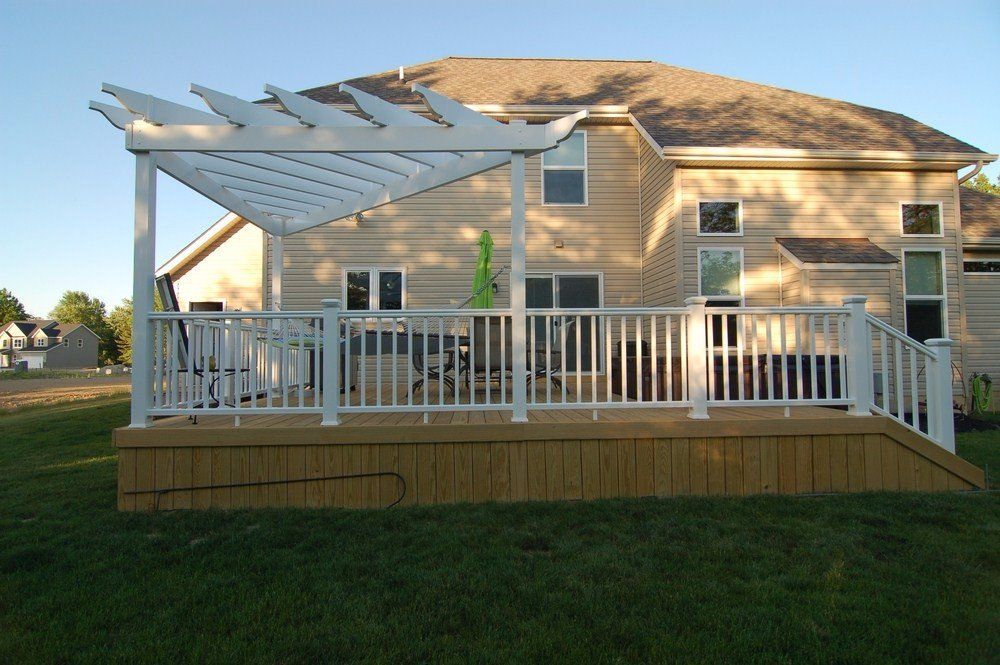 Back deck with white railing and pergola attached to a tan two-story house