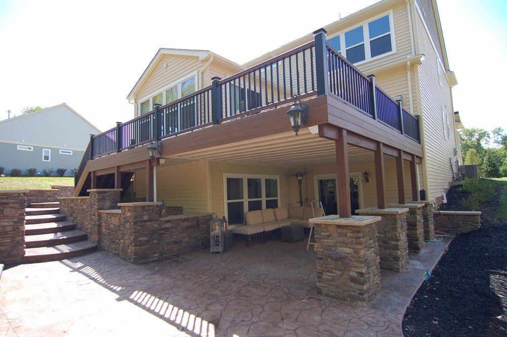 Raised deck on a beige house with stone support pillars and stairs in a sunny yard