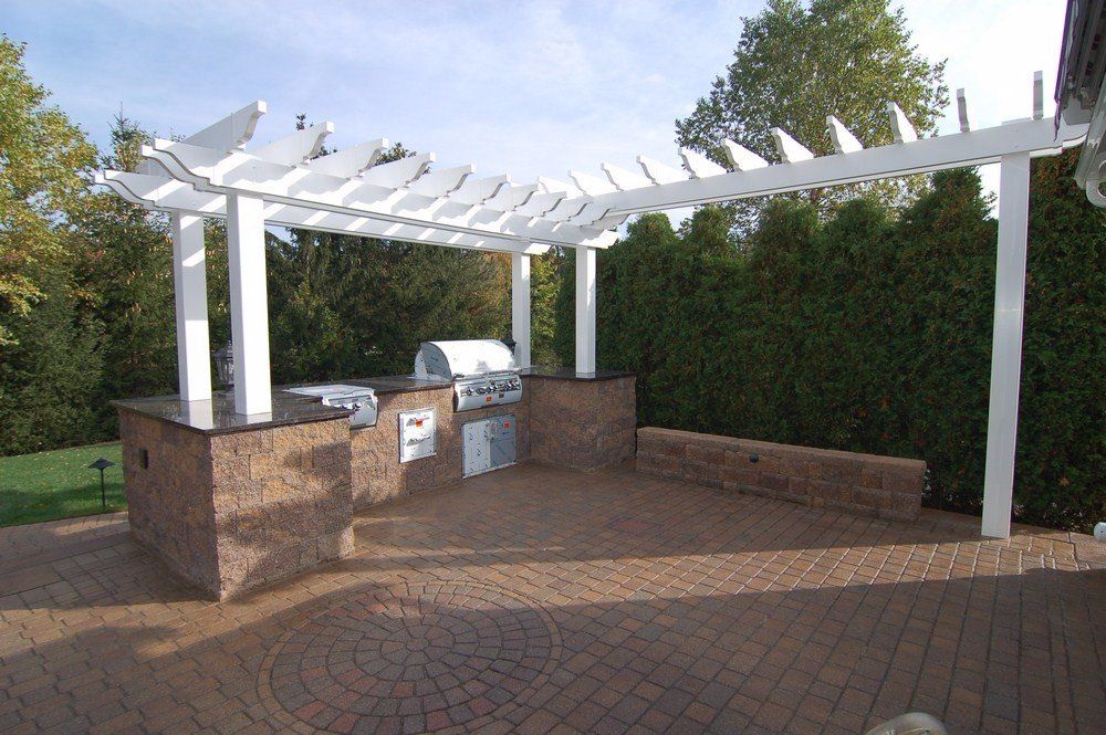 Outdoor brick barbecue area with white pergola and built-in benches on a paved patio