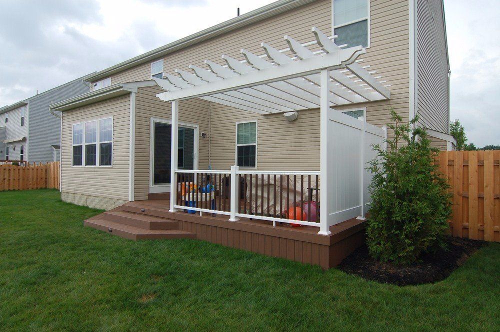 Backyard deck with white pergola, railing, and potted plants beside a beige house