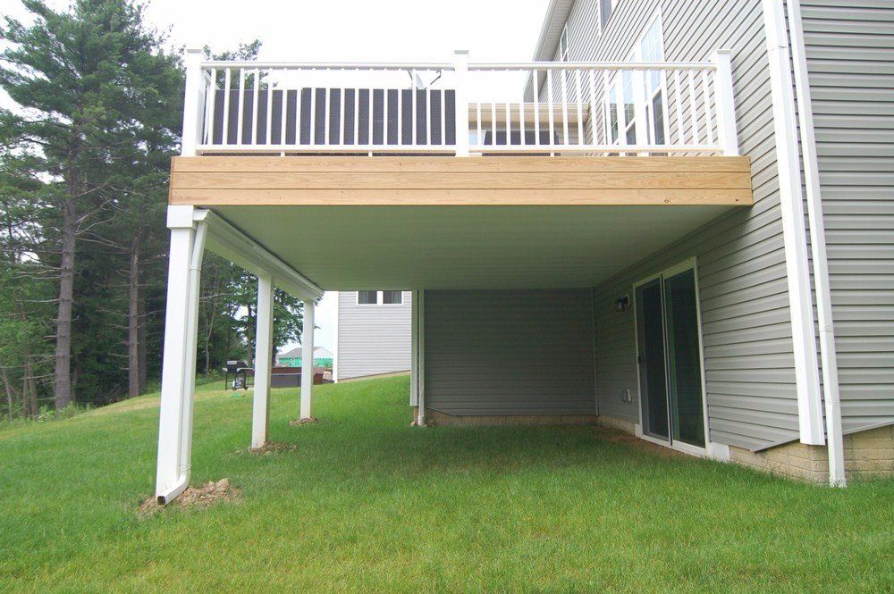 Backyard deck raised on white posts over a grassy lawn beside a house