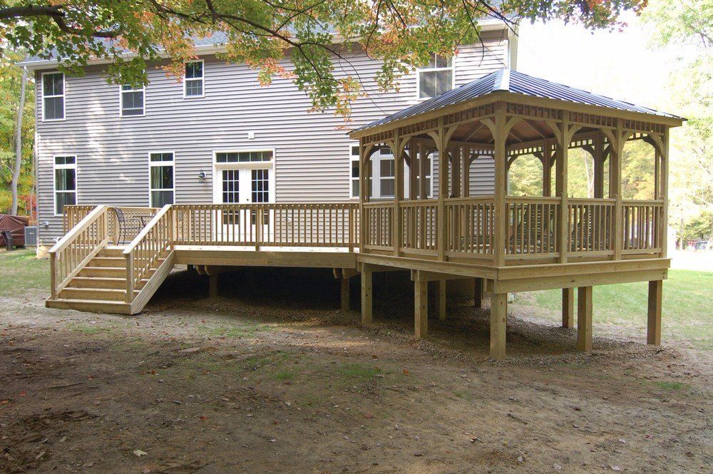 Wooden backyard deck and gazebo attached to a white house, with stairs on the left.