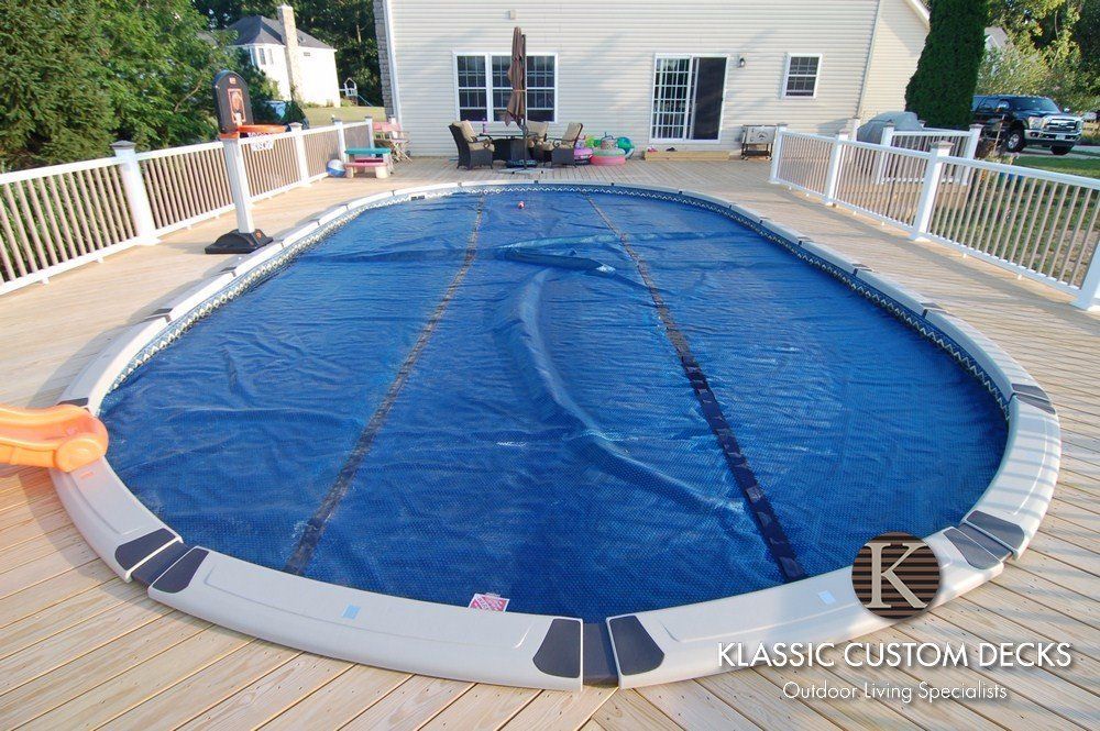 Covered backyard swimming pool surrounded by a wooden deck and white fence