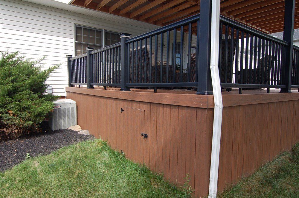 Brown deck with black railing beside a house, above a grassy yard.