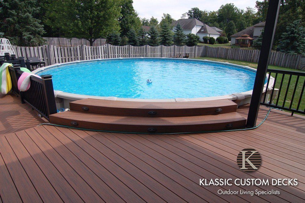 Backyard deck with a round above-ground pool and wooden steps, surrounded by a fence and trees