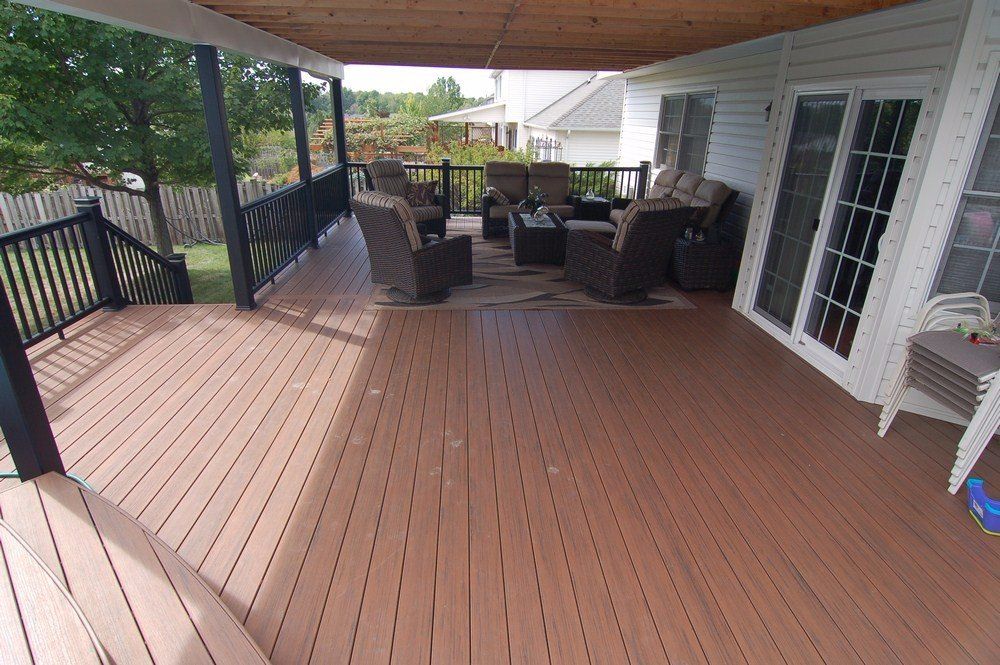 Covered wooden deck with brown flooring, black railing, and wicker patio furniture under a roofed porch