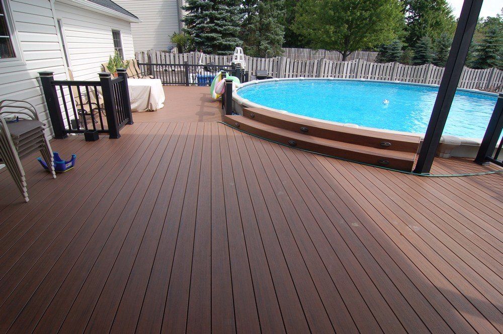 Wooden deck beside an above-ground pool, with patio furniture and a white house wall.
