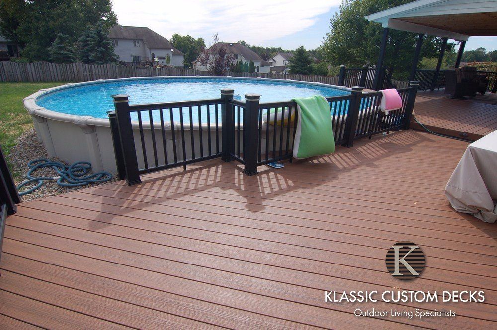 Backyard deck with above-ground pool and black fence, colorful towels draped over railing.