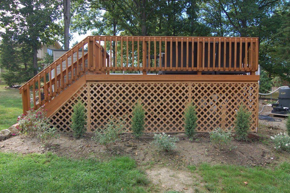 Wooden backyard deck with stairs, lattice skirting, and railing among trees and grass