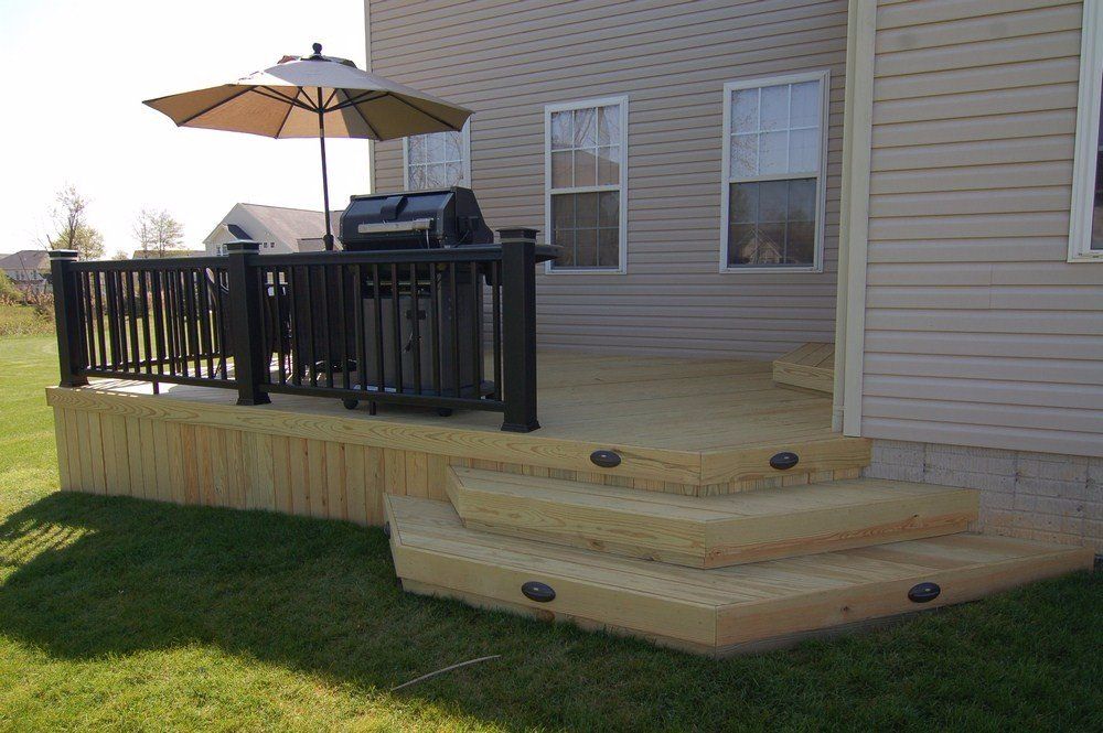 Backyard deck with black railing, umbrella, grill, and light wood steps leading to a grassy lawn