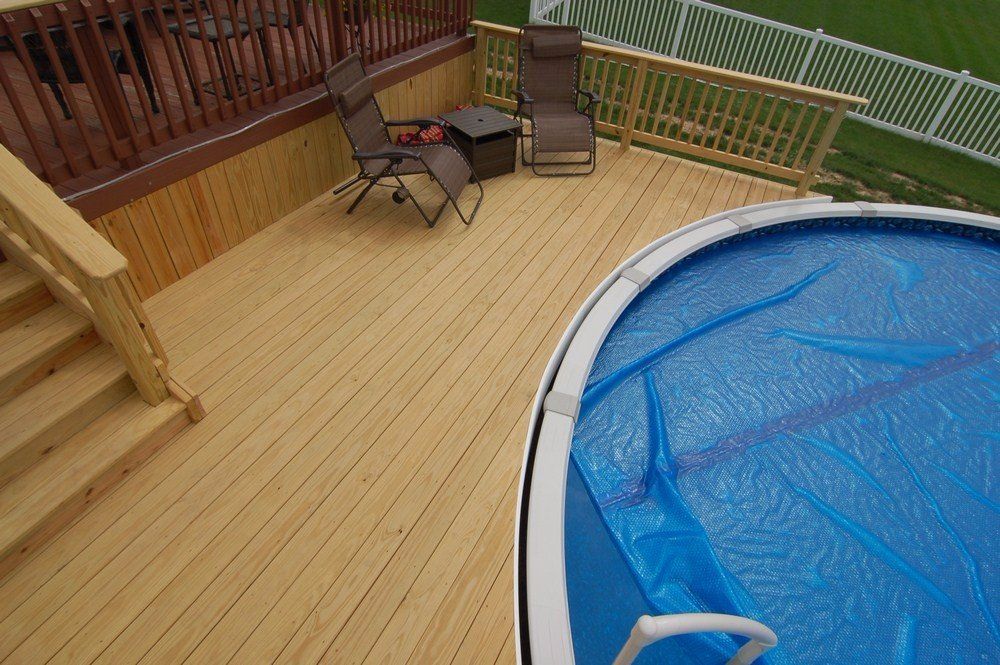 Wooden deck with patio chairs and a covered swimming pool beside stairs and railing