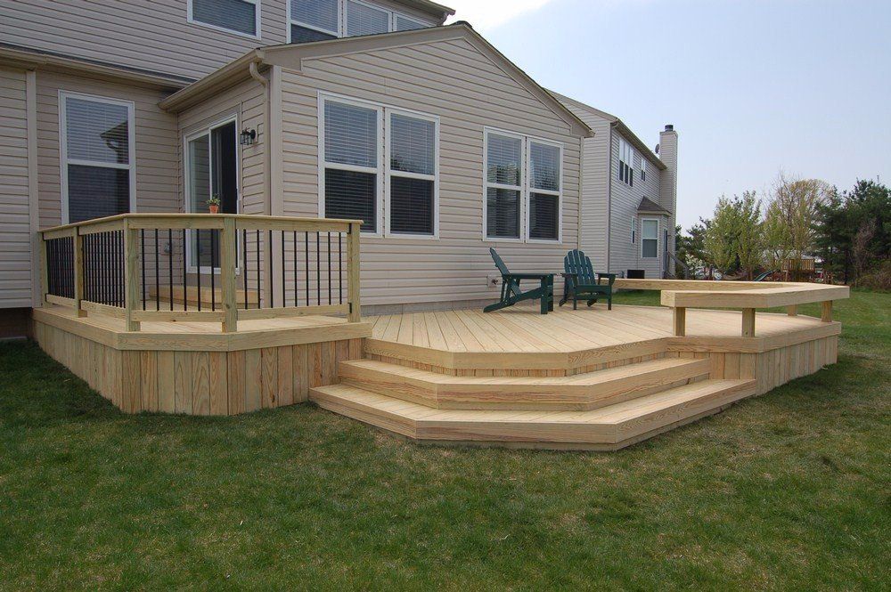 Wooden deck with steps and railing attached to a beige house, with two green chairs on the patio.