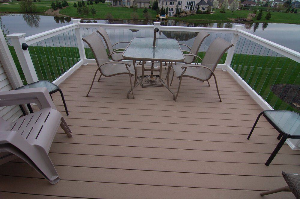 Patio with glass table and metal chairs on a wooden deck overlooking a green yard