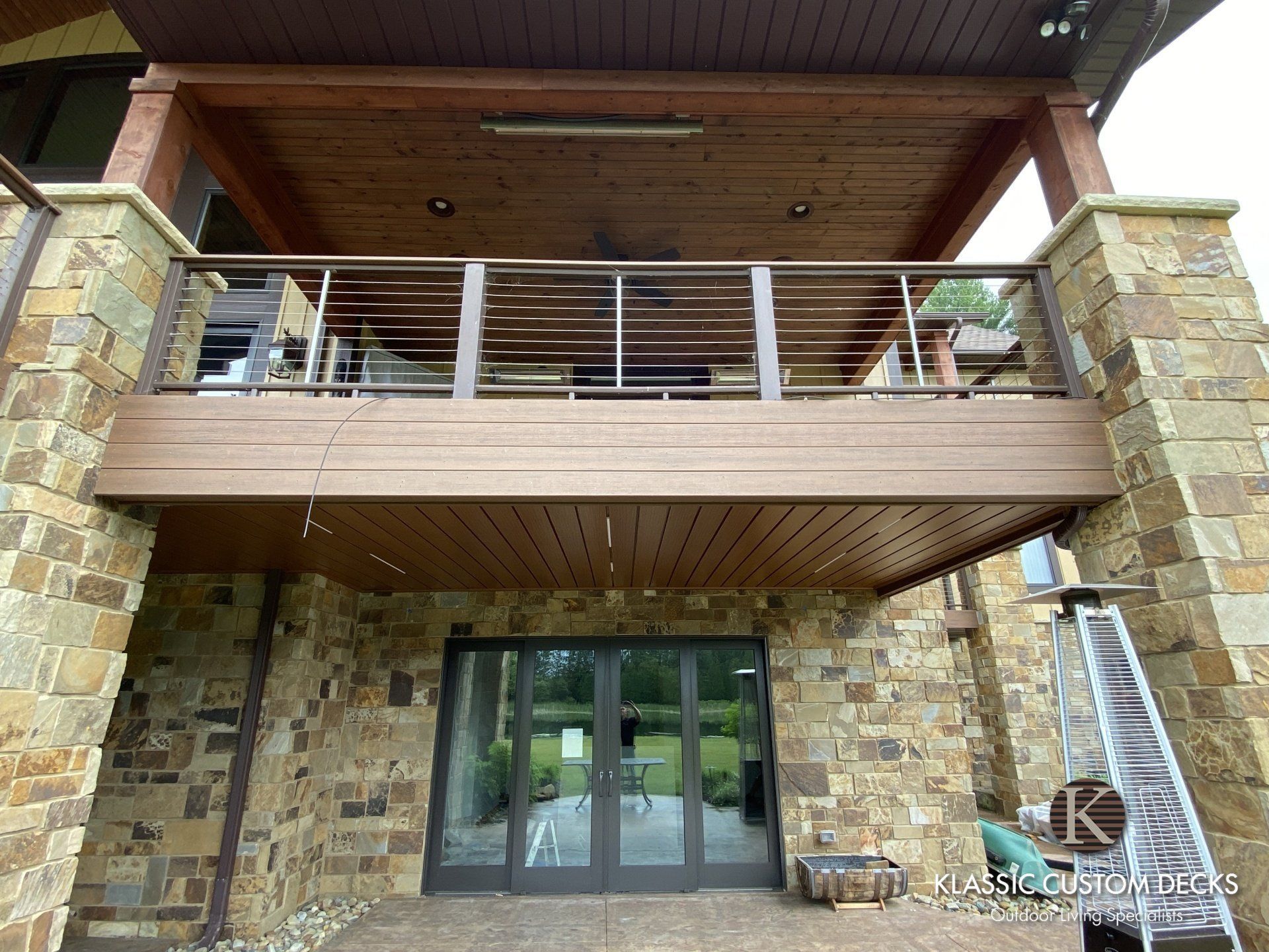 Stone building entrance with glass doors, upper balcony, and wood-paneled overhang