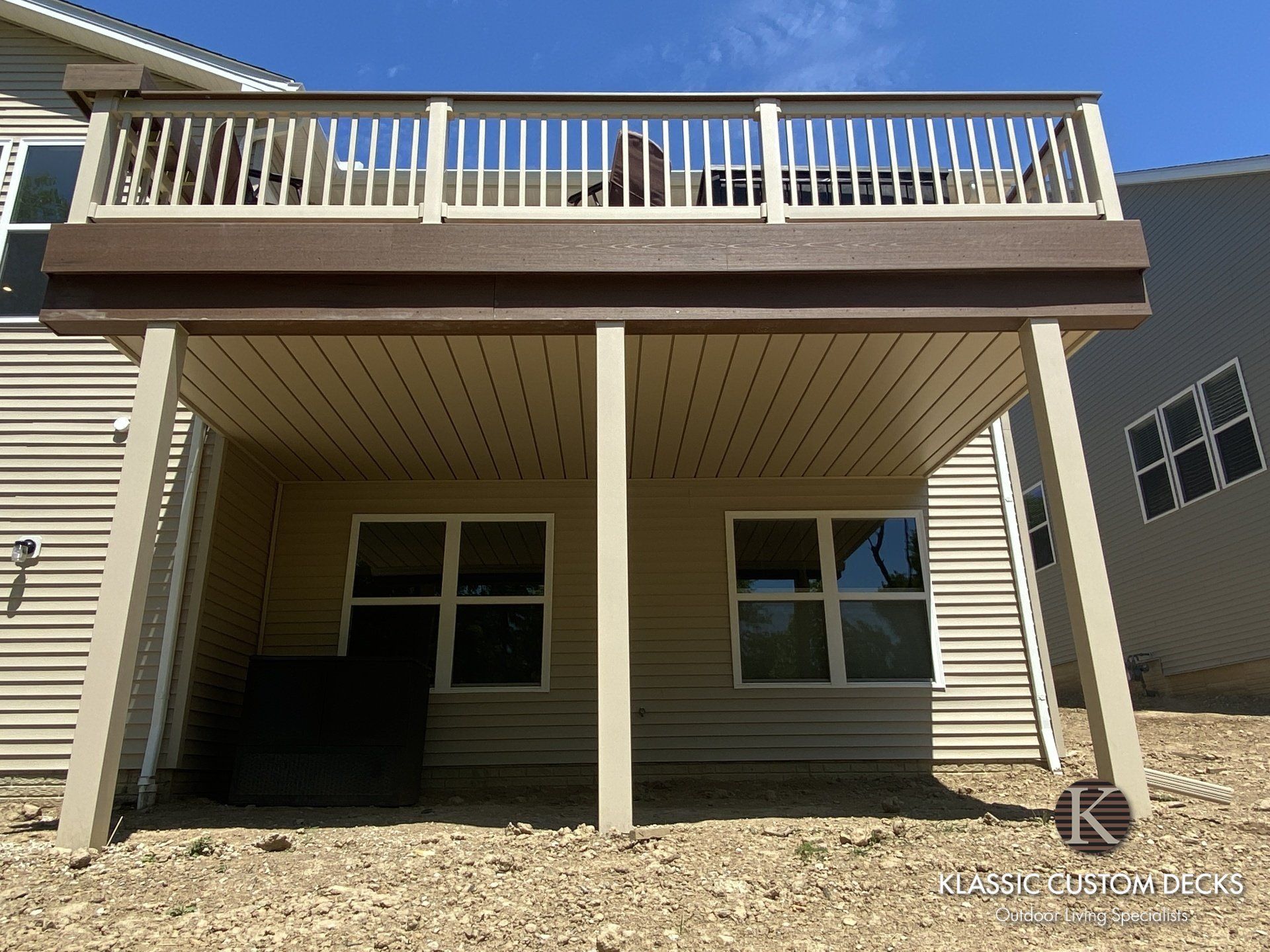 Raised backyard deck with white railing above a covered patio and shaded area underneath