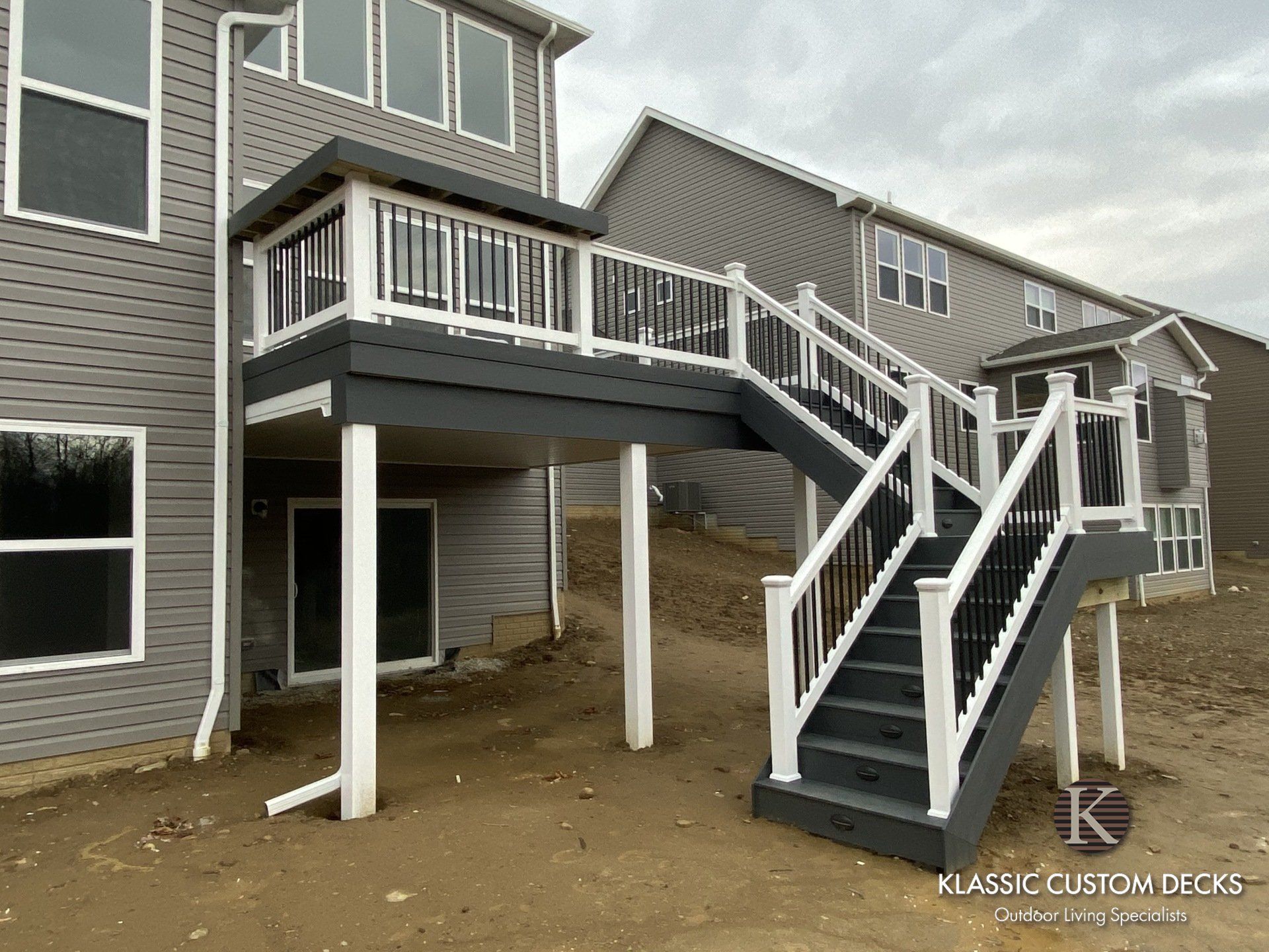 Raised wooden deck with stairs and support posts attached to a gray house under construction