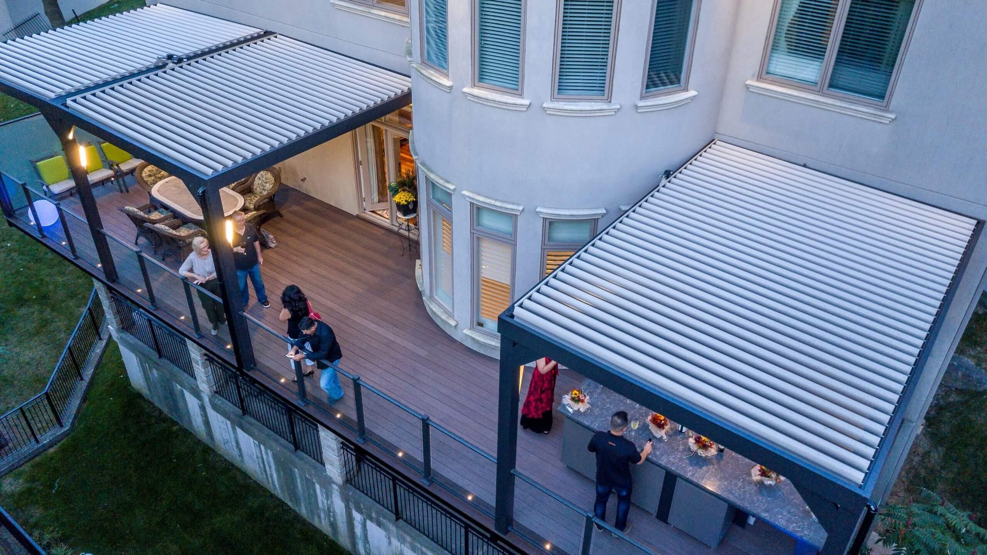 Two people on a balcony under striped awnings beside a curved white building at dusk