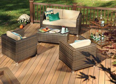 Outdoor wicker patio seating set with beige cushions, glass table, and potted plants on a wooden deck