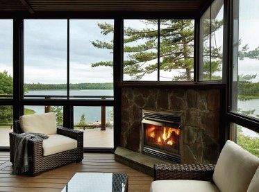 Cozy lakeside living room with fireplace, wicker chairs, and large windows overlooking water and trees