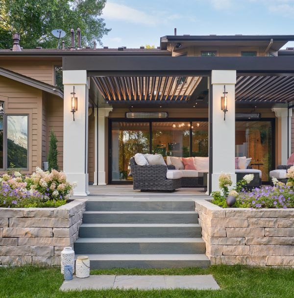 Modern house patio with steps, stone retaining walls, and a covered seating area with lights