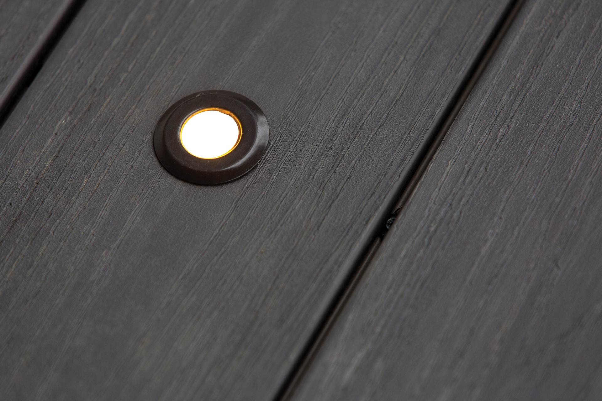 Close-up of a recessed round light glowing on dark wooden decking.