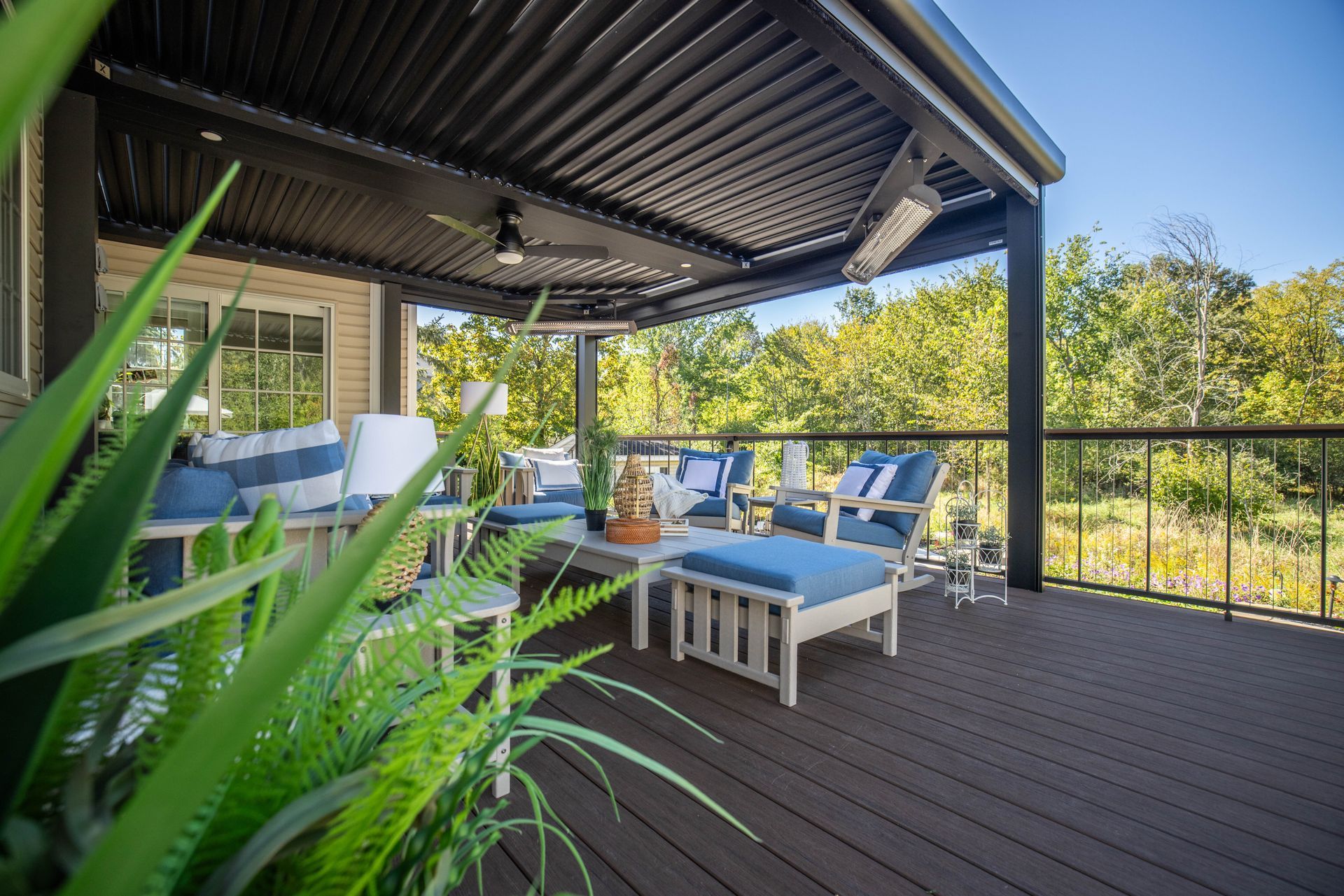 Covered patio with blue cushioned seating, white table, and wood deck overlooking trees and sky