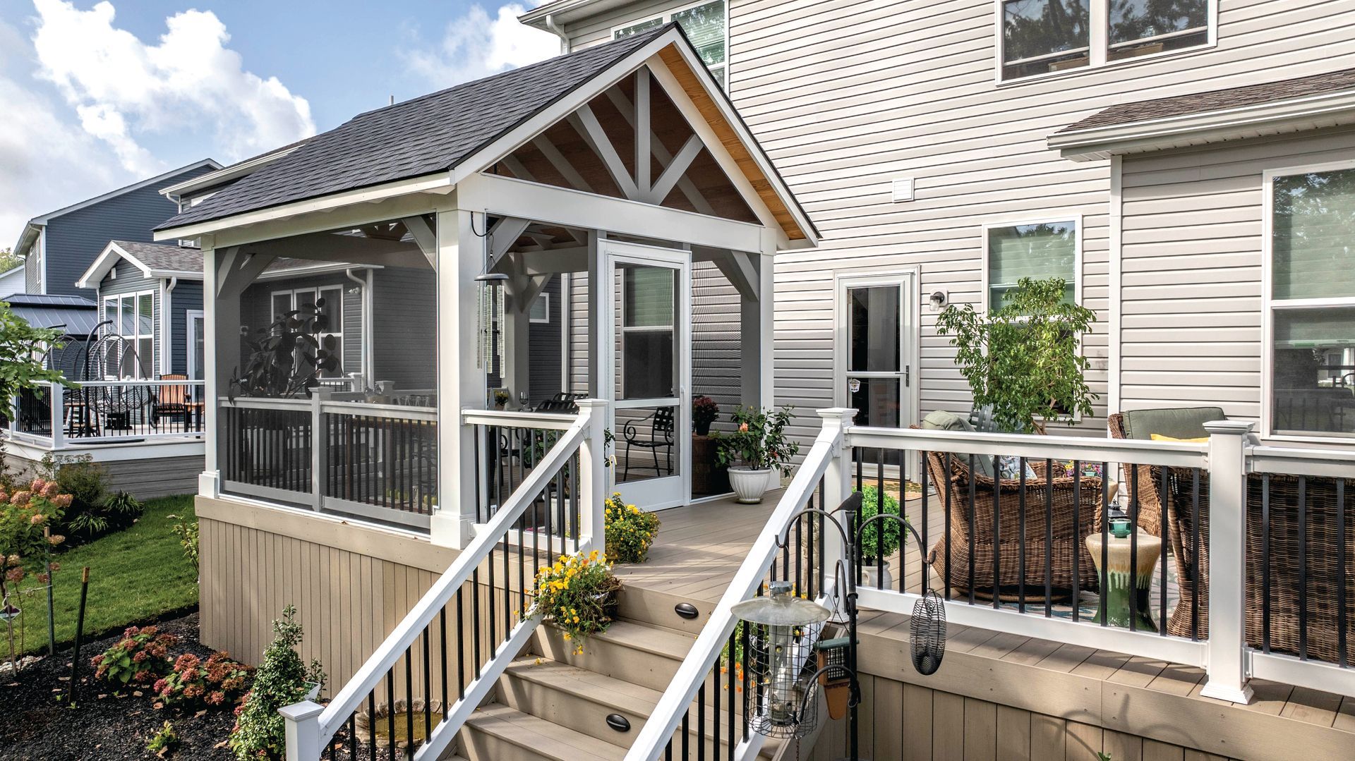Small screened porch with white railing and steps beside a beige house and flower boxes