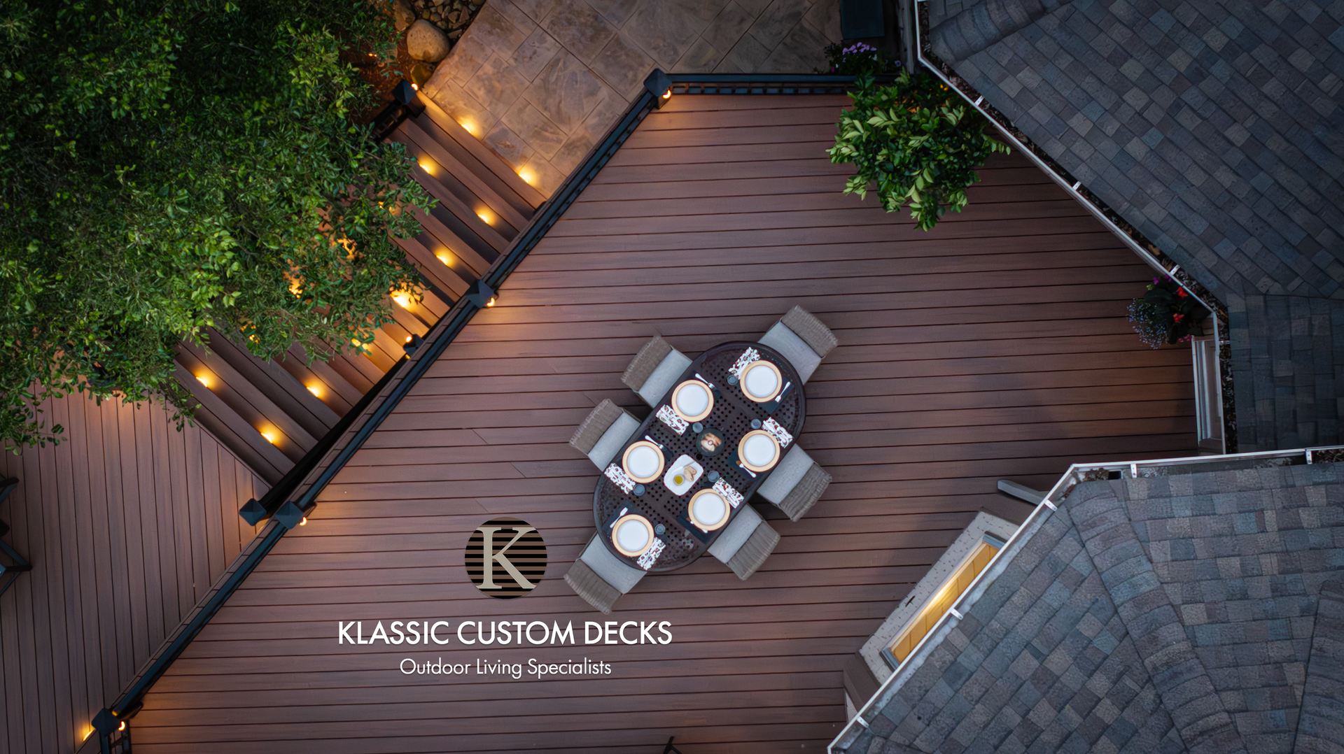 Top-down view of a custom wooden deck with outdoor dining set, string lights, and landscaping.