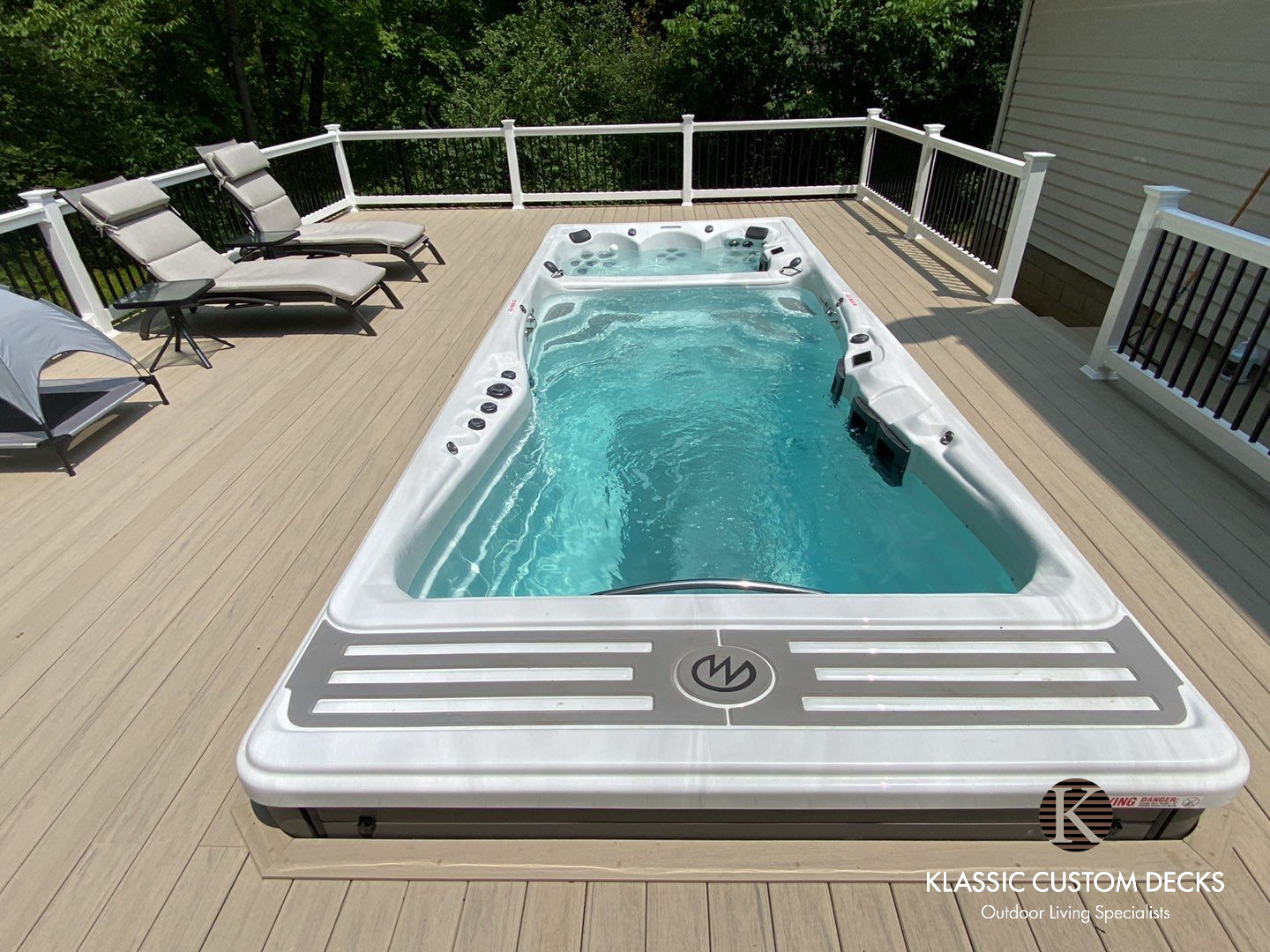 Backyard deck with a small in-ground pool, lounge chairs, and white railings in bright sunlight
