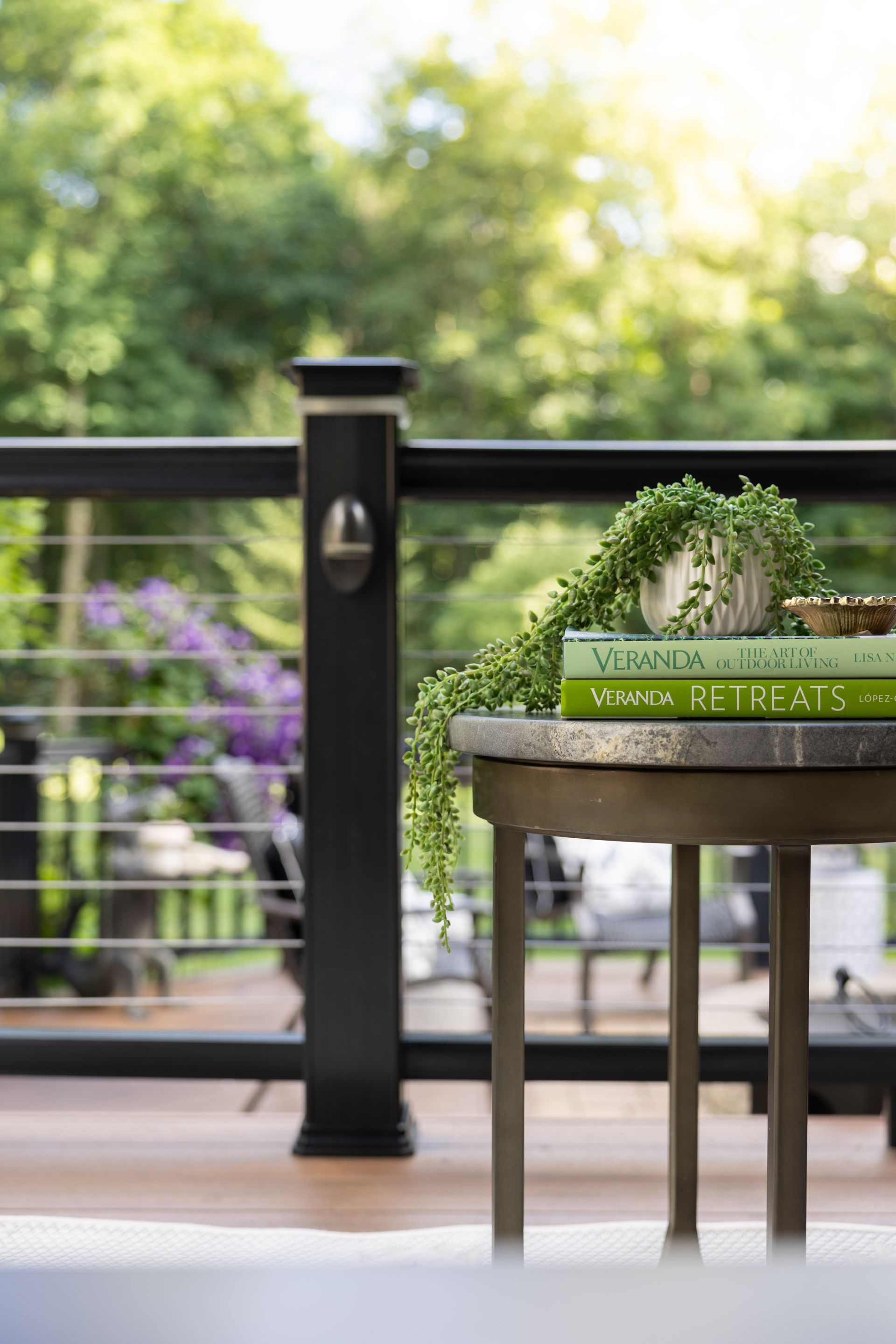 Patio table with green wreath and stacked books beside a black railing, with blurred garden in the background